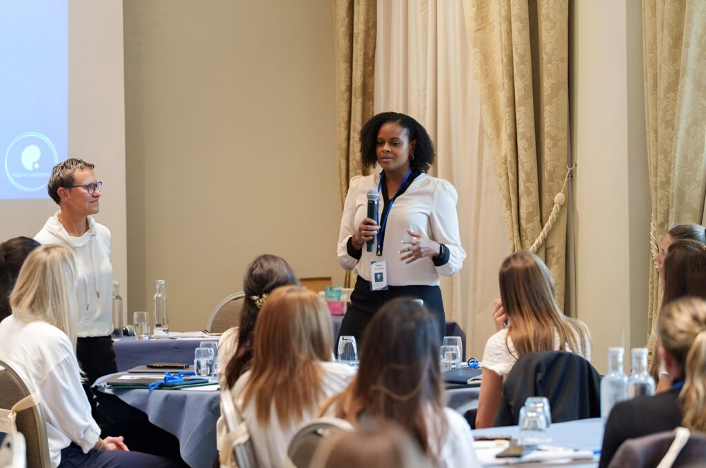 Amber Glasgow speaking with a microphone at the IOC/ASOIF Women's Leadership Workshop in Lausanne, Switzerland